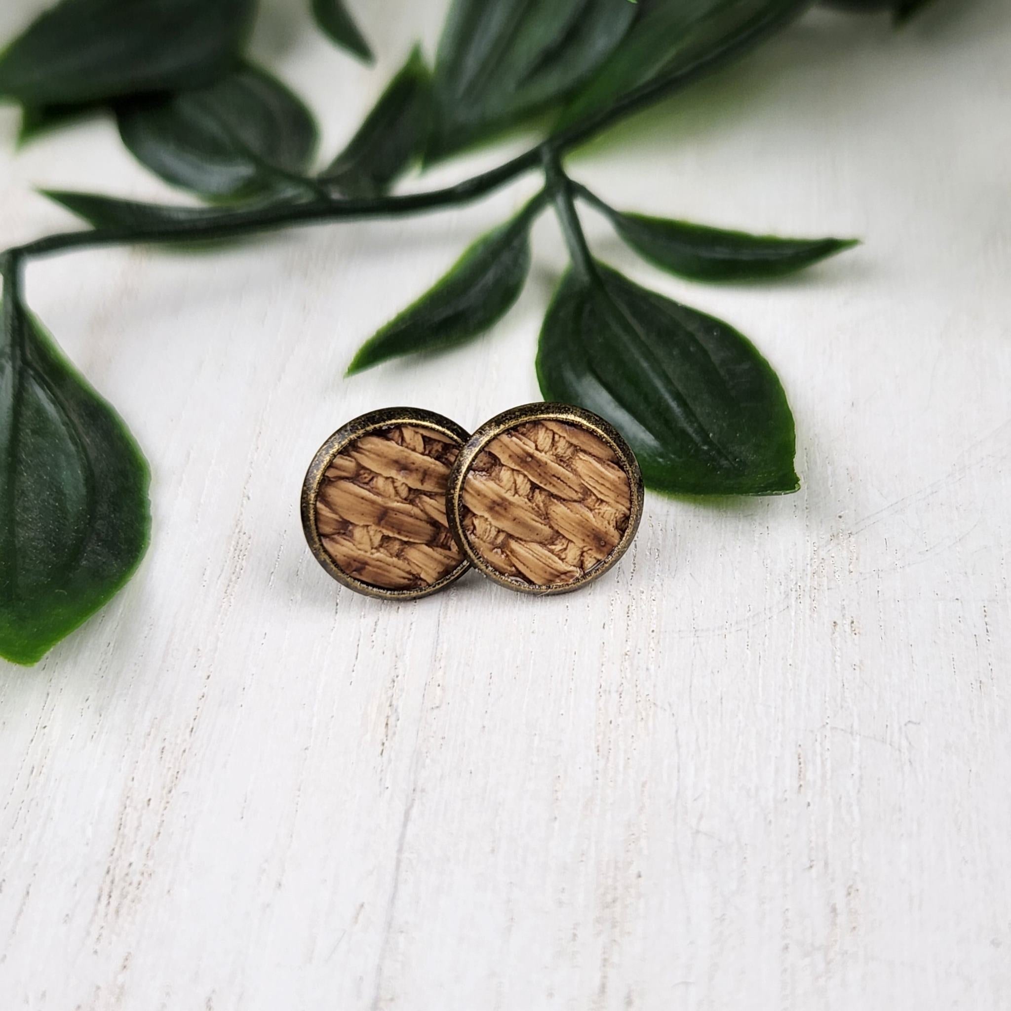 A pair of rustic, bronze plated stainless steel studs, Thy have a brown faux leather basket weave inlay.