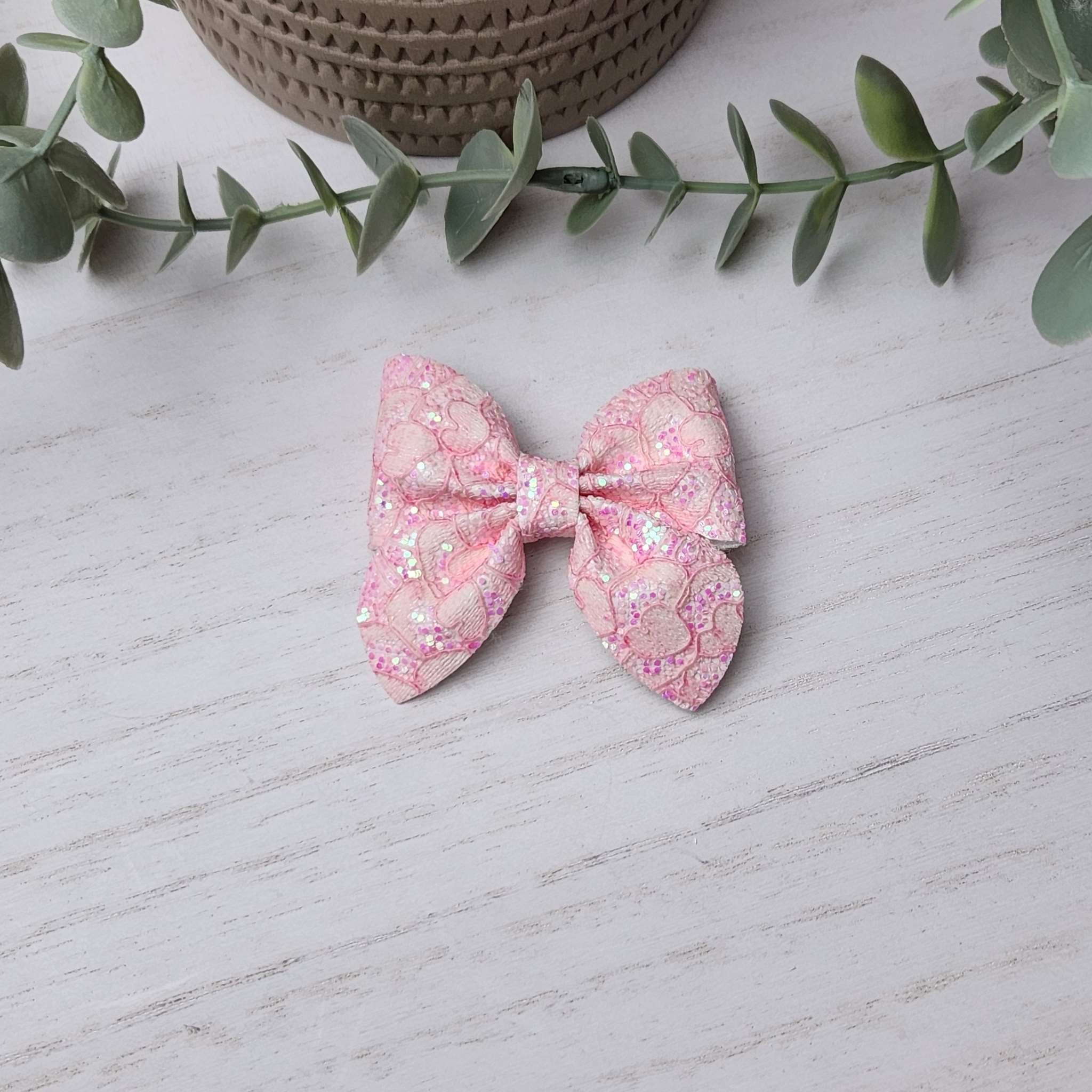 Pink glitter sailor bow made with faux leather, has an alligator clip to fasten to hair.