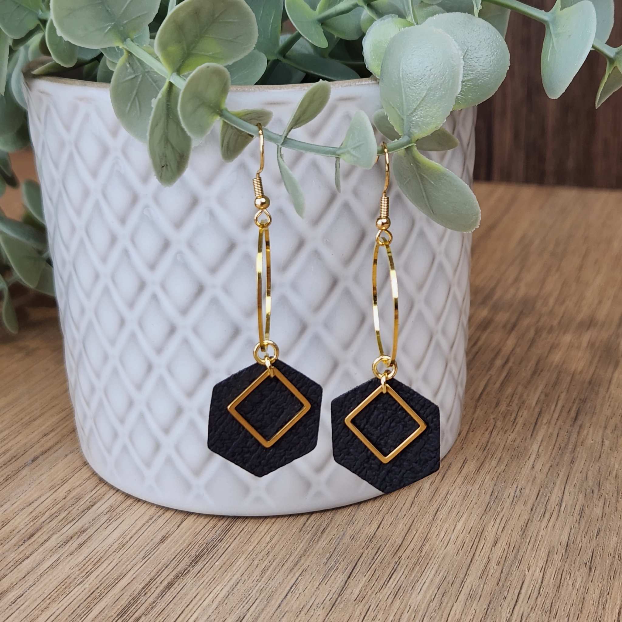 A pair of earrings made with a black faux leather, and gold plated hypoallergenic findings. The earrings are 70mm long.