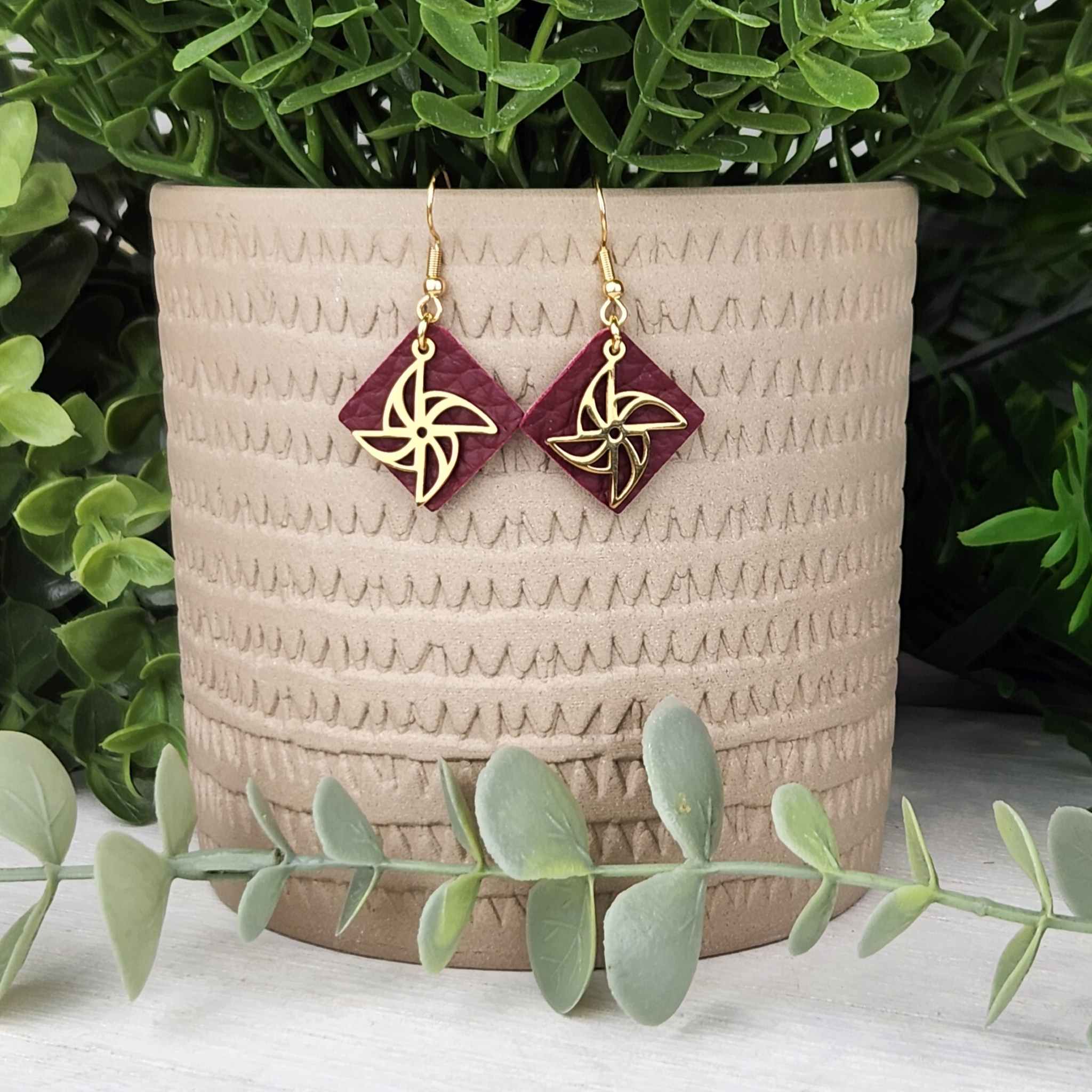 Gold pinwheel over wine red leather.  Made with hypoallergenic hooks.