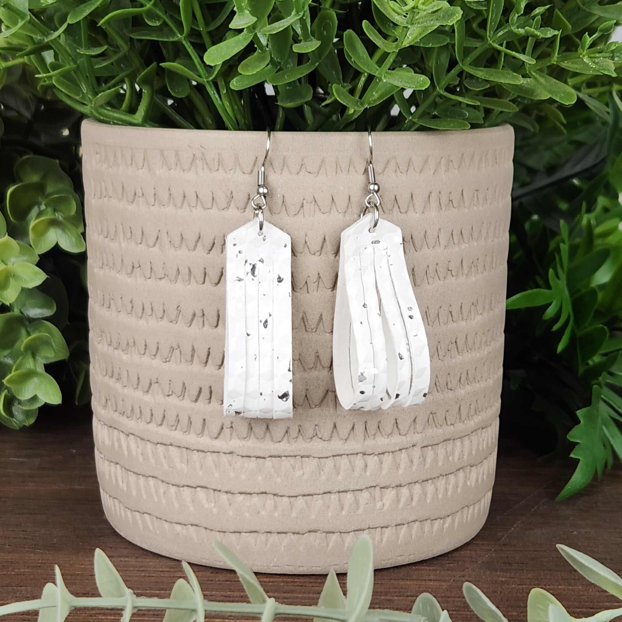 A silver speckled white faux leather earring. Has a silver ring above the leather portion.