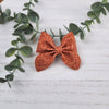 Orange sailor bow made with faux leather, has an alligator clip to fasten to hair.